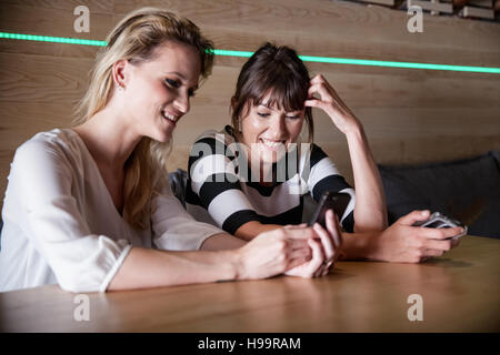Two women in coffee shop using their smartphones Stock Photo