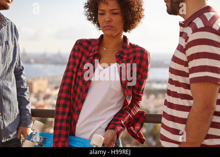 Thoughtful girl with blue skateboard wearing a white tank top, black and red squared shirt with male in a striped white and red t-shirt Stock Photo