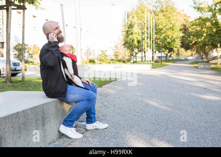 Father with baby girl in baby carrier using phone Stock Photo