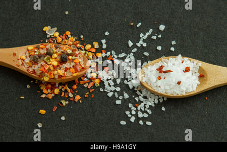 Two wooden spoons with spices and salt on black background Stock Photo