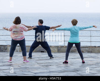 Mature man and two mature women practicing Tai chi overlooking the sea Stock Photo