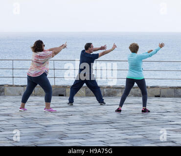 Mature man and two mature women practicing Tai chi overlooking the sea Stock Photo