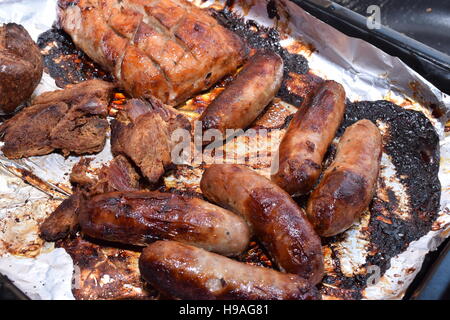 Selection of freshly cooked meat on tin foil in a black baking tray Stock Photo