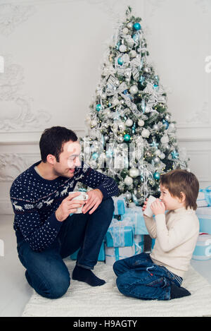 Happy dad and son with cups of tea talking near Christmas time at home Stock Photo