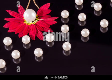 White pearls necklace on black background. Focus on the big pearl from the left corner over red petals! Stock Photo