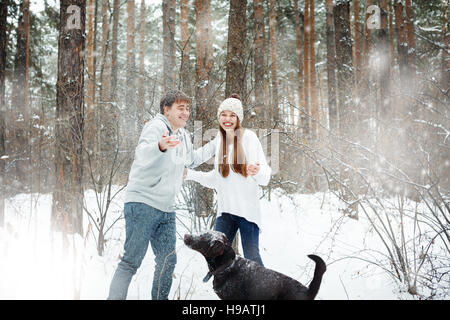 Young funny couple having fun in snowy forest with dog Stock Photo