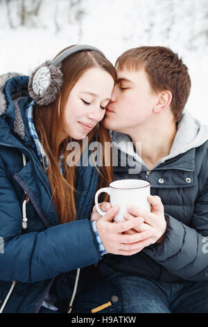 Loving couple having fun outdoors in winter, holding big cup with hot tea Stock Photo