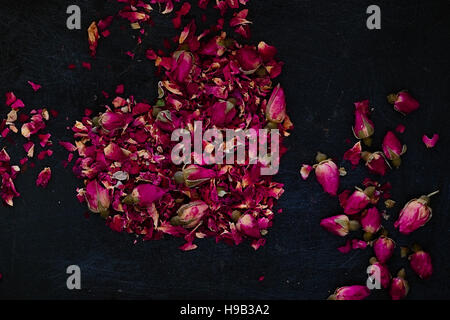 Dried rose petals and buds in a heart shape on a dark background. Romantic ingredient for tea, bath or cosmetics. Dark food photography. Horizontal Stock Photo