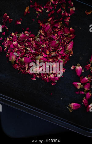 Dried rose petals and buds in a heart shape on a dark background. Romantic ingredient for tea, bath or cosmetics. Copy space. Dark food photography Stock Photo