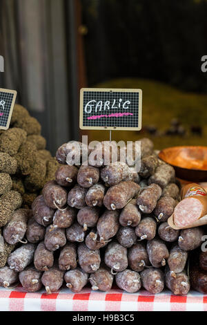 Specialty sausages for sale on stall at farmers market, piled high on red gingham cloth with handwritten blackboard sign Stock Photo