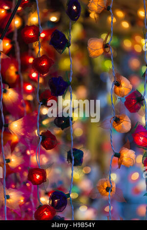 Strings of colored lights in floral orchid shapes, blurred bokeh background, christmas market cafe Stock Photo