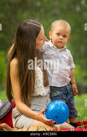 Happy young woman sat in park with baby boy. Stock Photo