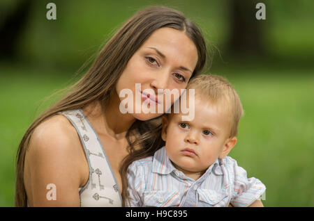 Happy young woman sat in park with baby boy. Stock Photo