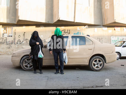 Shiite couple with veiled face in front of a car covered with mud decorated for ashura  commemoration, Lorestan province, Khorramabad, Iran Stock Photo