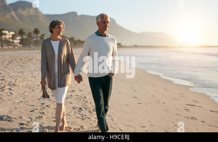 Shot of senior couple walking along beach together holding hands. Stock Photo