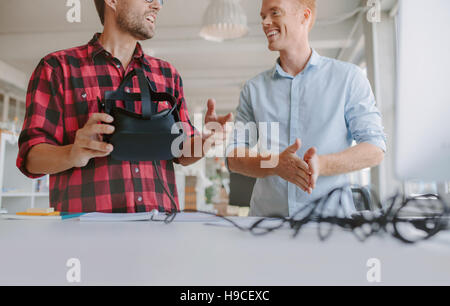 Cropped shot of two young men testing virtual reality headset. Business men discussing and testing VR glasses. Stock Photo