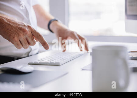 Close up shot of young man hands typing on wireless keyboard on desk in office. Stock Photo