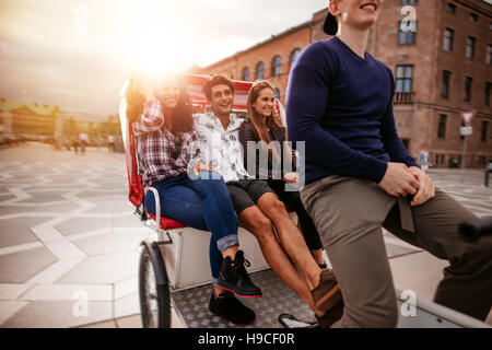 Teenage friends enjoying tricycle ride. Teenagers riding on tricycle in city and having fun. Stock Photo