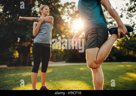 Shot of young man and woman stretching in the park. Young couple warming up in morning. Stock Photo