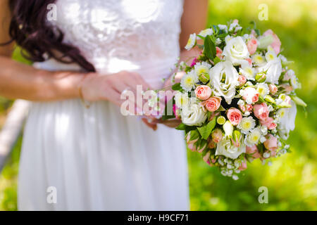 Bride holding a wedding bouquet with roses on a green background during the summer Stock Photo