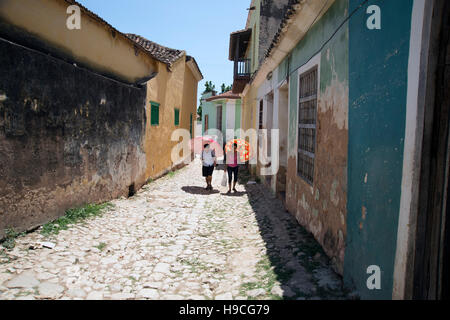 Two Cuban women walking up an old cobbled street in Trinidad Cuba using umbrellas as shade from hot sun Stock Photo