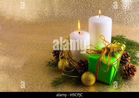 Glowing white Christmas candles, green gift box, golden balls, fir branches and cones on a gold background, horizontal, copy space Stock Photo