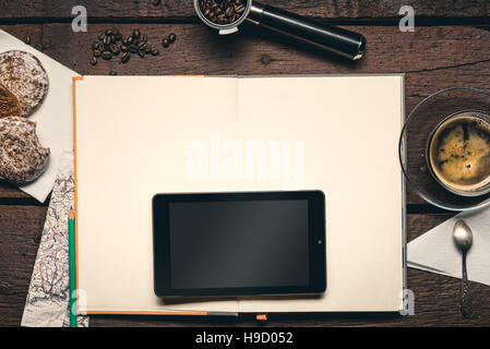 Tablet on blank pages of notepad on the wooden table, cup od coffee, cakes, map and beans. Stock Photo