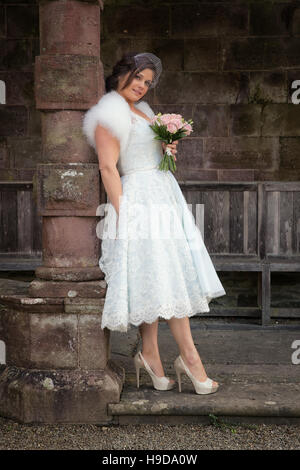 Lady in vintage wedding gown leans against a stone pillar Stock Photo