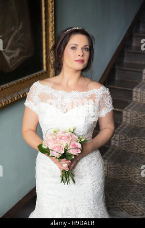 Bride in lace bridal gown holds pink bouquet, vertical format Stock Photo