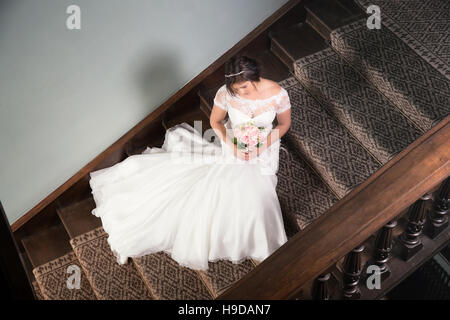 Bride sat on the stairs with her wedding dress fanned out Stock Photo