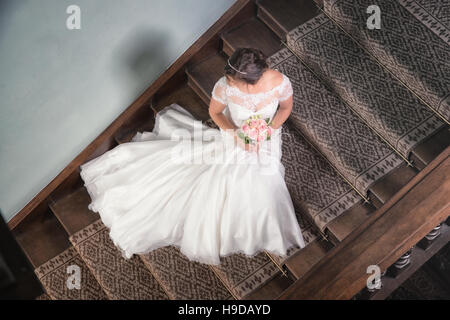 Bride sat on the stairs with her wedding dress fanned out.  Looking down from above to the beautiful bride in her wedding gown. Stock Photo