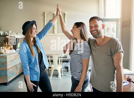 Three people in light room and two women making high five gesture while man smiling away. Stock Photo