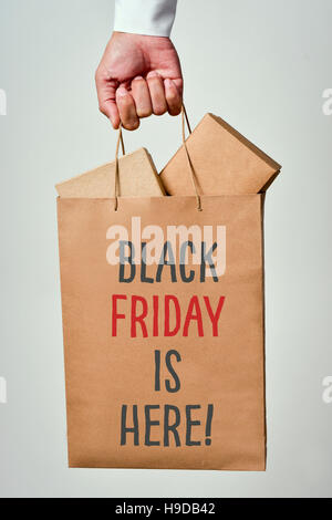 closeup of the hand of a young caucasian man holding a paper shopping bag full of cardboard boxes and the text black friday is here written in it Stock Photo