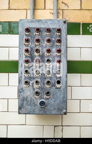 An electrical box containing red lights and switches mounted on a white tiled wall. Stock Photo