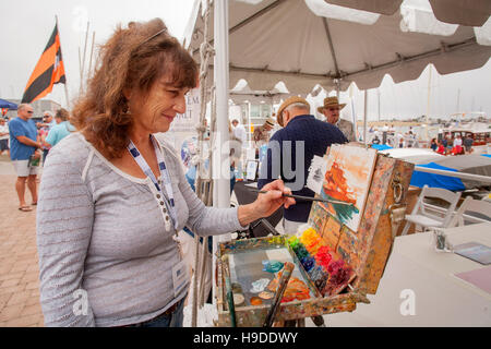 A Caucasian woman marine artist works at her easel in a Newport Beach, CA, yacht club boat yard depicting a vessel in the harbor. Note colorful paints. Stock Photo