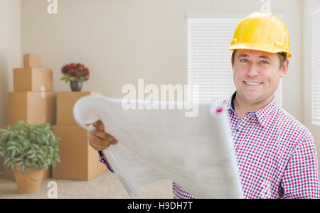 Happy Male Construction Worker In Room With Moving Boxes Holding Roll of Blueprints. Stock Photo