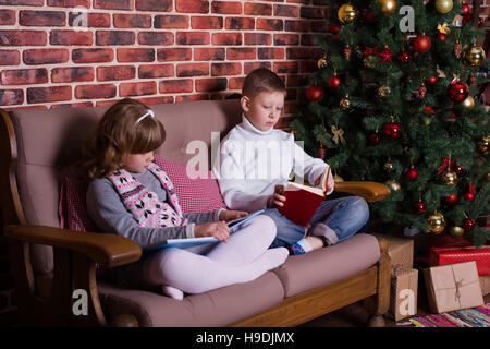 Boy and girl reading book on the sofa near the Christmas tree Stock Photo