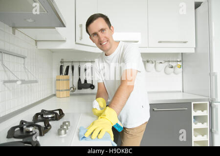Young smiling man wearing rubber gloves cleaning the stove Stock Photo