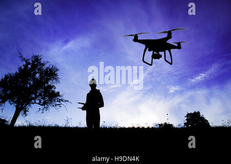 Silhouette of man with flying drone in nature at dusk. Stock Photo
