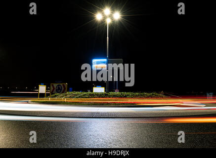 A dark roundabout at night near the TT circuit in Assen, the Netherlands. Passing cars create beautiful light trails. Stock Photo