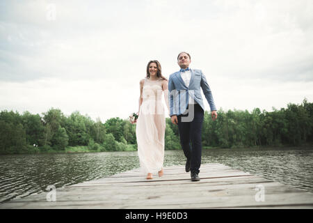 elegant stylish groom with his happy gorgeous brunette bride on the background of a lake Stock Photo