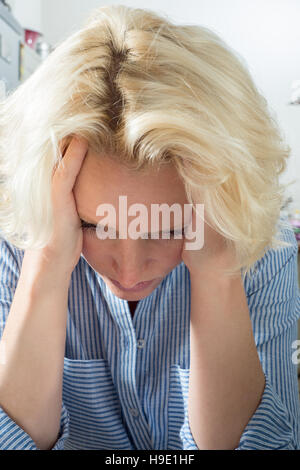 Female blonde lady holding head in hands looking worried Stock Photo