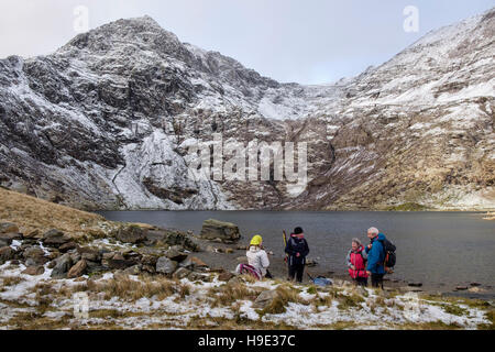 Hikers resting by Glaslyn lake below Mount Snowdon peak with snow in winter.  Snowdonia National Park (Eryri). North Wales UK Britain Stock Photo