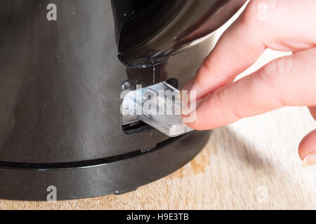 Close up shot as two fingers press down the switch to turn on and boil a black kettle on a wooden table or surface Stock Photo