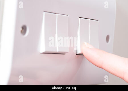 A manicured finger is about to turn on one of the lights by pressing a switch on a white 4 gang light switch Stock Photo