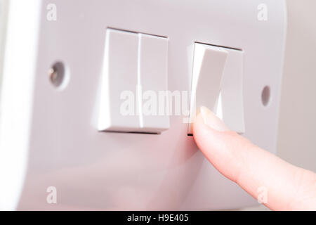 A manicured finger has just turned a light by pressing a switch on a white 4 gang light switch Stock Photo