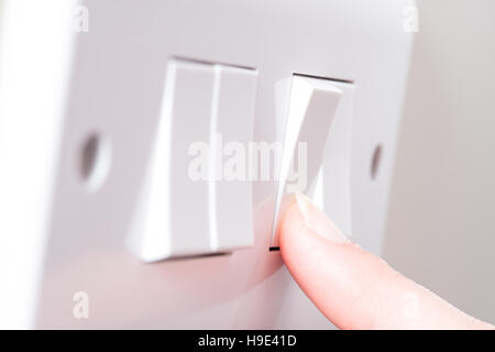 A manicured finger has just switched on a light by pressing a button on a white 4 gang light switch Stock Photo