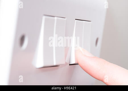 A manicured finger about to swithc on a light by pressing a switch on a white 4 gang light switch Stock Photo