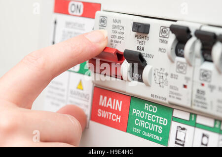 A finger is about to switch off a large red MAINS switch on an RCD circuit breaker board Stock Photo