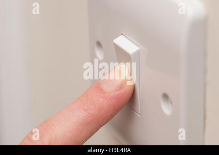 Close up. A finger presses down on a single white light switch on a cream wall. COPY SPACE Stock Photo